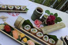 sushi is served in wooden containers on a table with flowers and other food items