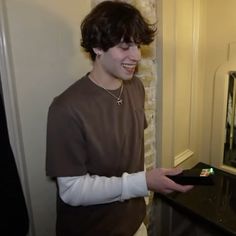 a young man standing in front of a mirror holding a remote control and smiling at the camera