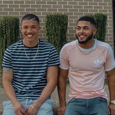 two young men sitting next to each other on a bench in front of a brick building