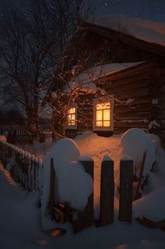 a log cabin with snow on the ground and windows lit up in the night sky