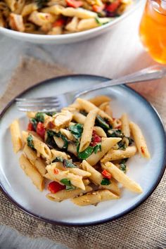 pasta with spinach and red peppers on a plate next to a glass of orange juice