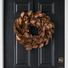 a wreath hanging on the front door of a house with black doors and gold trim