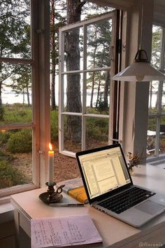 an open laptop computer sitting on top of a desk next to a candle and window