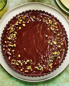 a chocolate tart with pistachios on top sits on a white plate