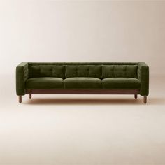 a green velvet couch with wooden legs on a plain surface, in front of a white wall