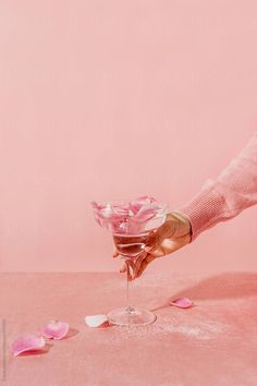 a person holding a martini glass with pink petals on the table by luma studio for stocksy magazine