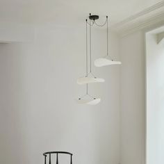 three lamps hanging from the ceiling in a room with white walls and flooring, along with a black chair