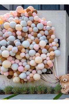 a teddy bear sitting in front of a giant balloon tree on the side of a building