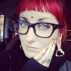 a woman with red hair and piercings on her face wearing black eyeglasses