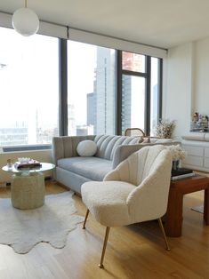 a living room filled with furniture next to large windows and a wooden floor covered in white rugs