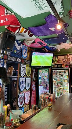 a man sitting at a bar in front of a large screen tv with flags hanging from the ceiling