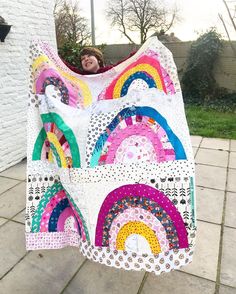 a woman is holding up a quilt made with rainbows and dots on the fabric