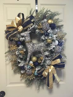 a christmas wreath on the front door with blue and gold ornaments hanging from it's side