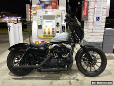 a motorcycle is parked in front of a gas pump at night, with no one around it