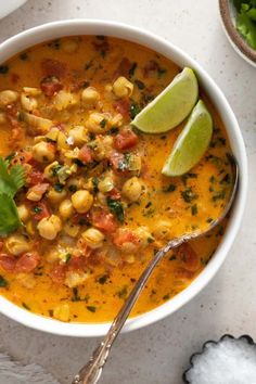 a white bowl filled with soup and garnished with cilantro, lime wedges