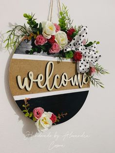 a welcome sign hanging from the side of a wall with flowers and greenery on it