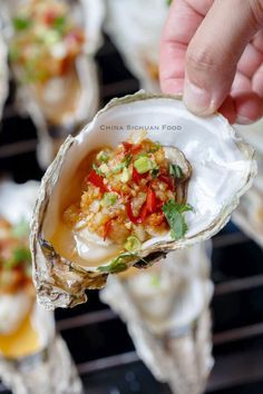 a person holding an open oyster on a grill with other food items in the background