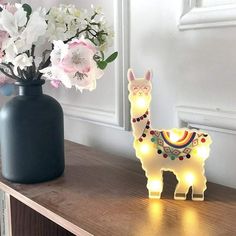 a light up llama sitting on top of a wooden table next to a vase filled with flowers