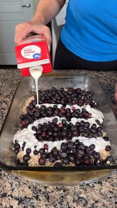 a person pouring milk on top of a blueberry pie in a glass baking dish