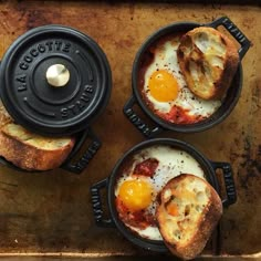 three breakfast dishes in cast iron pans on a wooden tray with one egg and two slices of bread