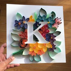 a person holding up a card with the letter k made out of paper flowers and leaves