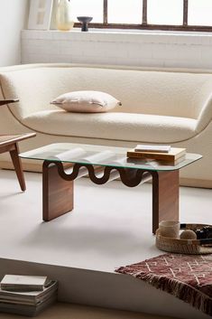 a white couch sitting next to a glass table on top of a wooden floor in front of a window