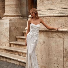 a woman in a white dress leaning against a stone wall with her hand on the ledge