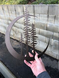 a hand holding up a metal sculpture with trees on it