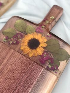 a wooden cutting board with a painted sunflower on the front and side of it