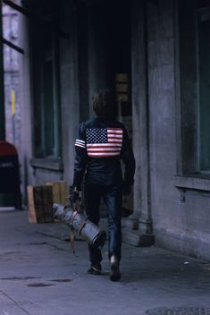 a man walking down the street with an american flag on his jacket and carrying a fire extinguisher