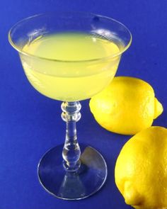 a glass filled with lemonade next to two lemons on a blue tablecloth