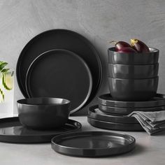 black plates and bowls are stacked on top of each other in front of a vase with flowers