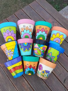 there are many colorful cups sitting on the wooden table together, all painted with different designs