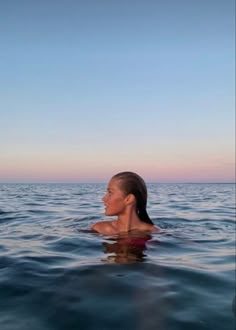 a woman swimming in the ocean with her head above the water's surface, looking up into the sky