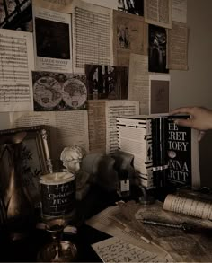 a table topped with lots of books next to a wall covered in old fashioned papers