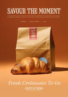 a bag of fresh croissants sits on the ground in front of an advertisement for savour the moment