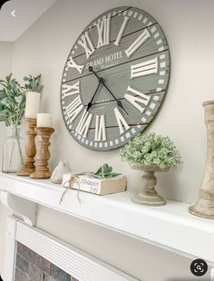 a clock on the wall above a mantle with candles and vases next to it