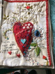 a red heart on a white cloth with flowers and words written in the center is surrounded by buttons