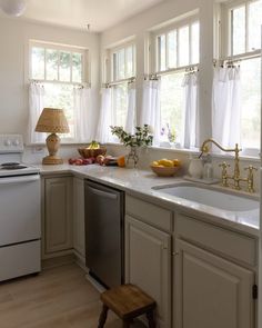 a kitchen with white walls and wooden floors has an oven, dishwasher, sink, and window