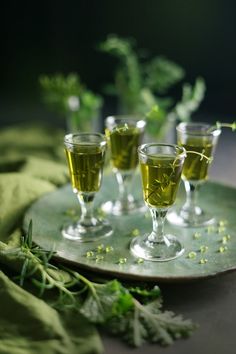 three glasses filled with green liquid sitting on top of a plate next to some herbs