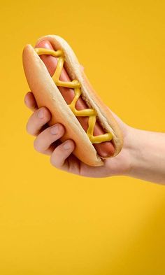 a hand holding a hot dog with mustard on it