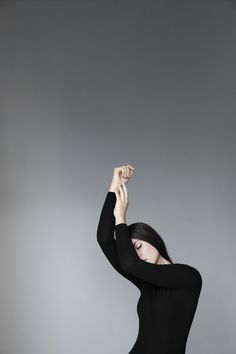 a woman in a black bodysuit is holding her hands up to the side with one hand