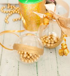 two glass ornaments with gold ribbon and ribbons around them on a white wooden table next to a can