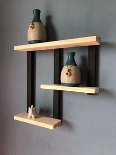 two wooden shelves with vases on them against a gray wall, one has a small white rabbit figurine