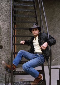 a man sitting on top of a set of stairs wearing a cowboy hat and jeans