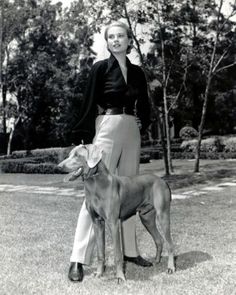 a black and white photo of a woman standing next to a dog in the grass