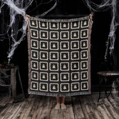 a woman standing in front of a black and white blanket with an intricate design on it