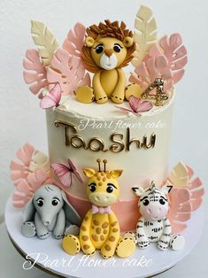 a cake decorated with animals and leaves on top of a white table topped with pink flowers