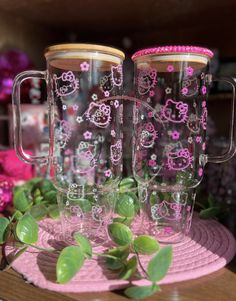 two hello kitty glass mugs sitting on top of a pink plate next to flowers