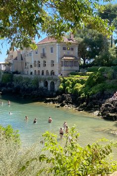 people are swimming in the water near a large house